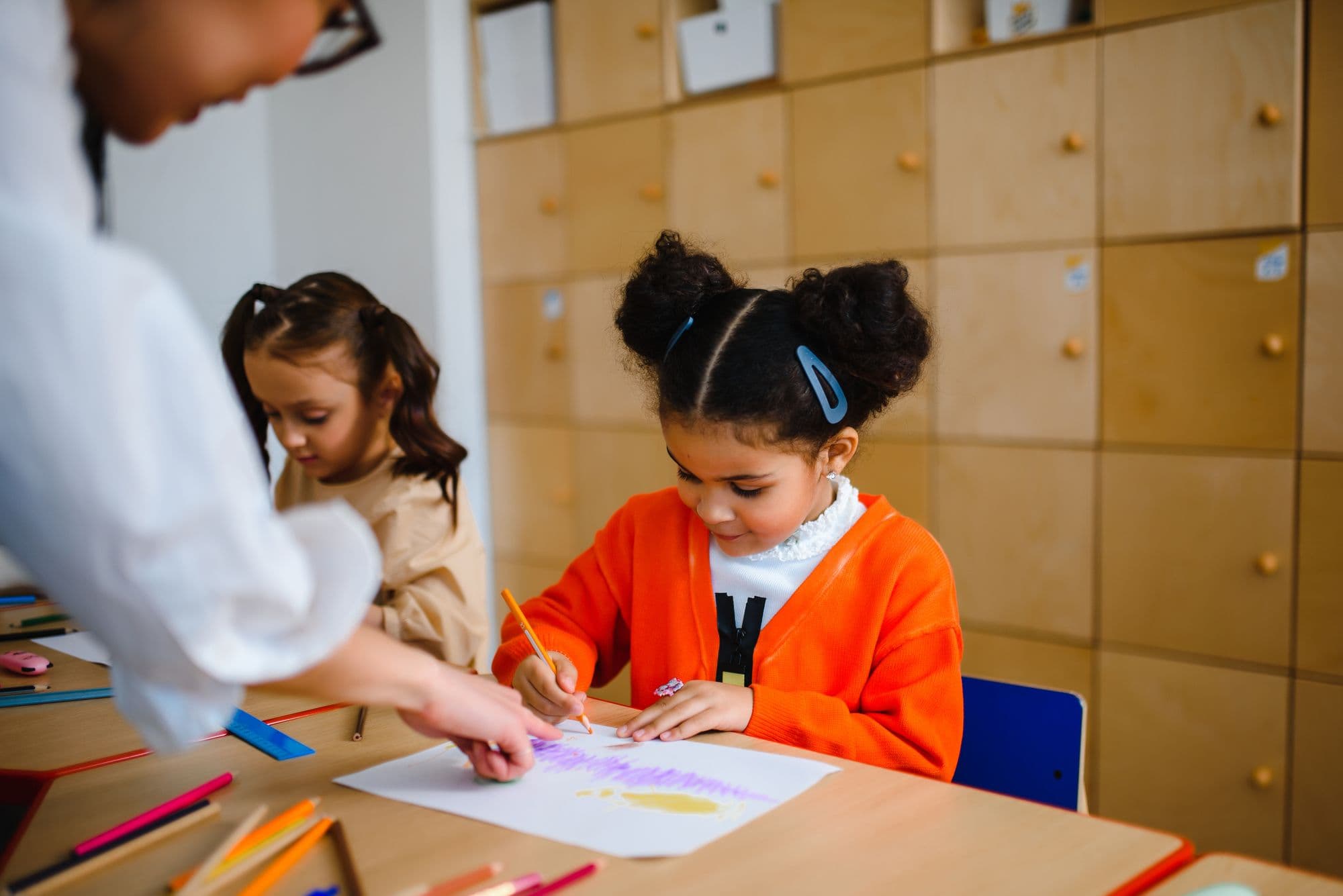 A girl draws in felt-tip at a shared table while other children work alongside her