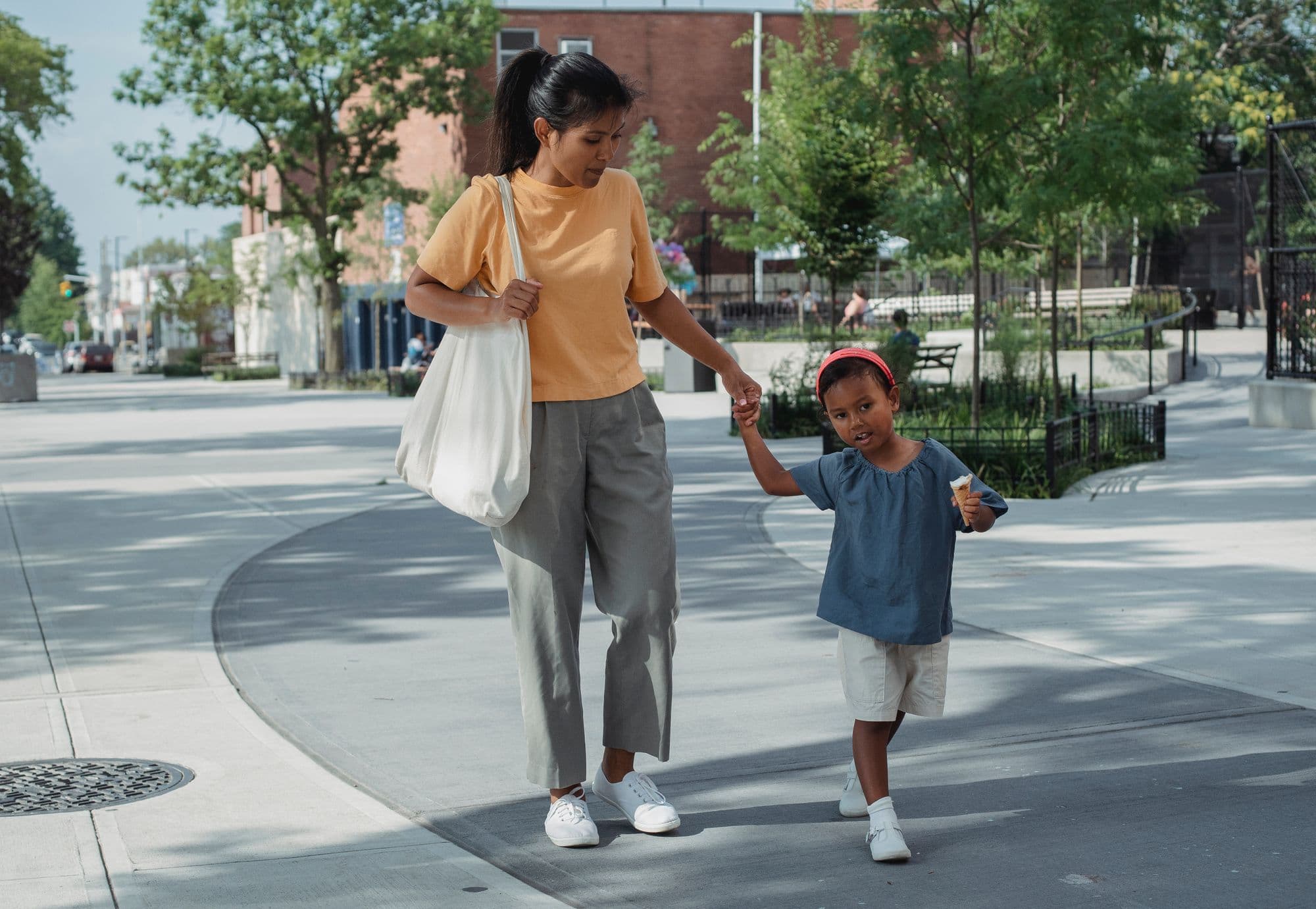 An adult and a young child walk hand in hand along a wide tree-lined pavement