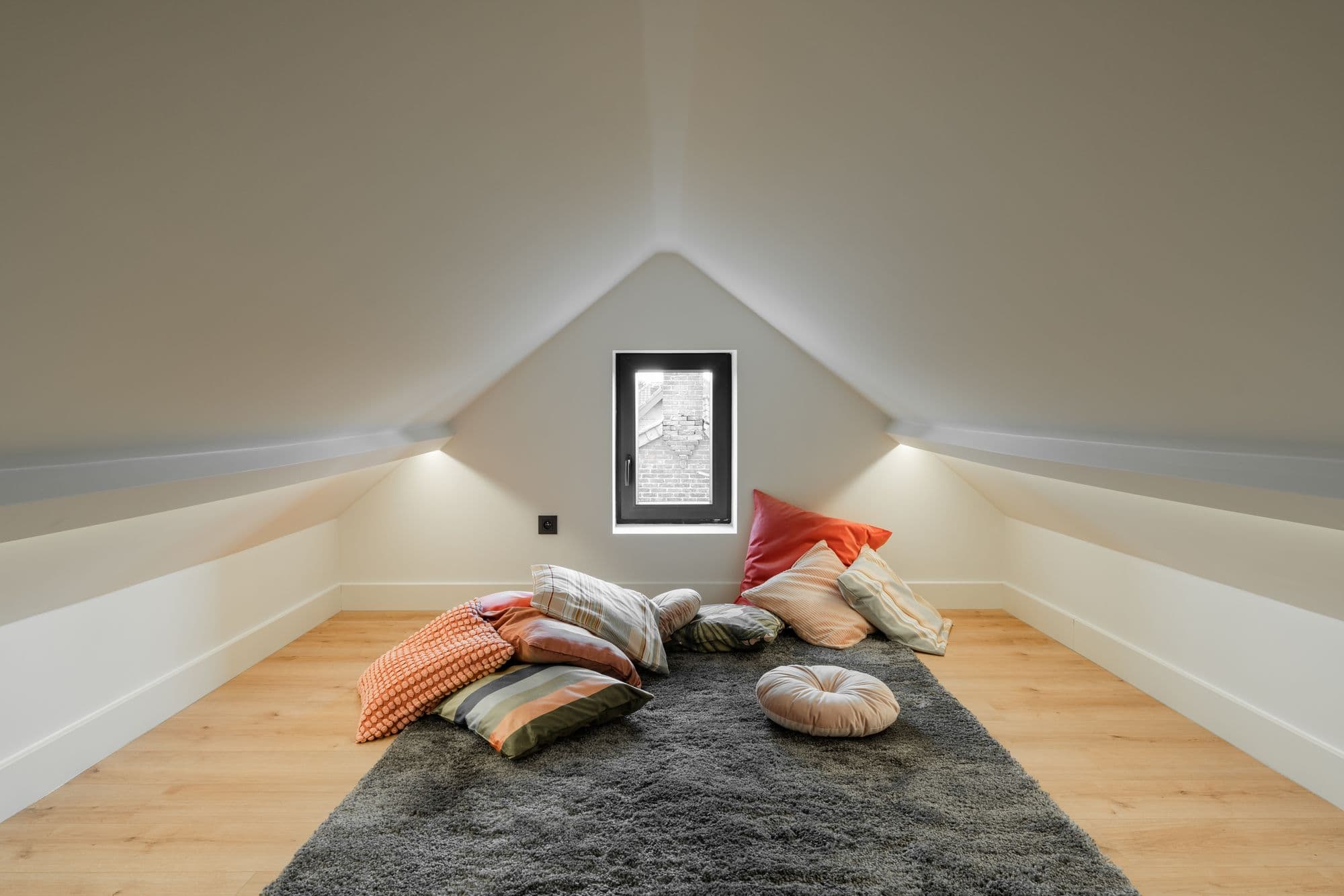 Floor cushions and a deep rug in a quiet, softly lit room under the eaves