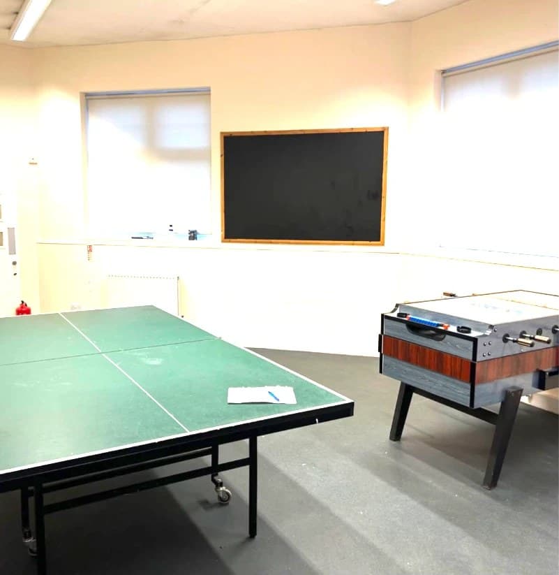 A table tennis table and an air hockey table in the daylit games room at Chesham Youth Centre, with a blackboard on the far wall