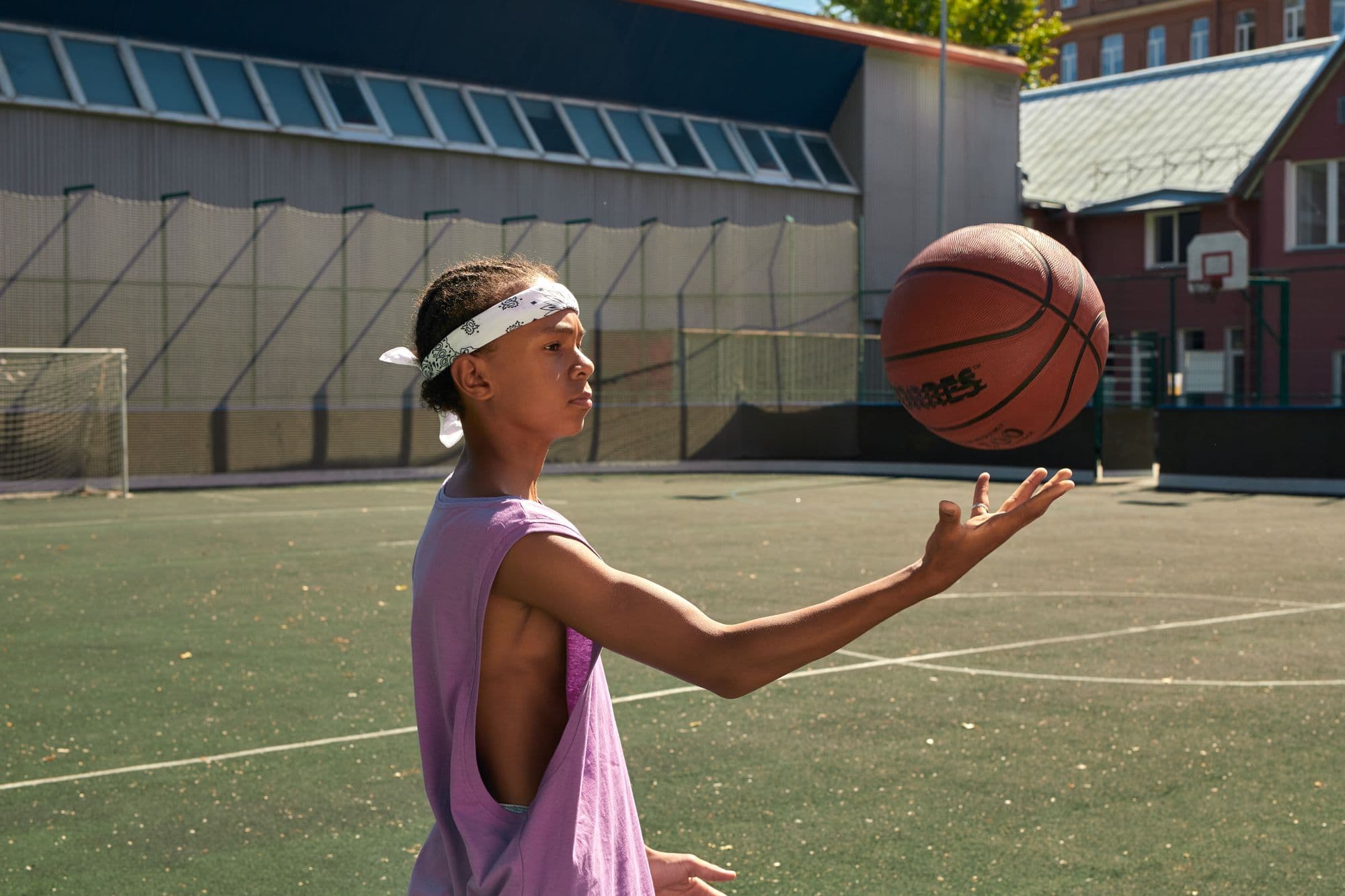 A girl in a headband balances a basketball on her fingertips on an outdoor court