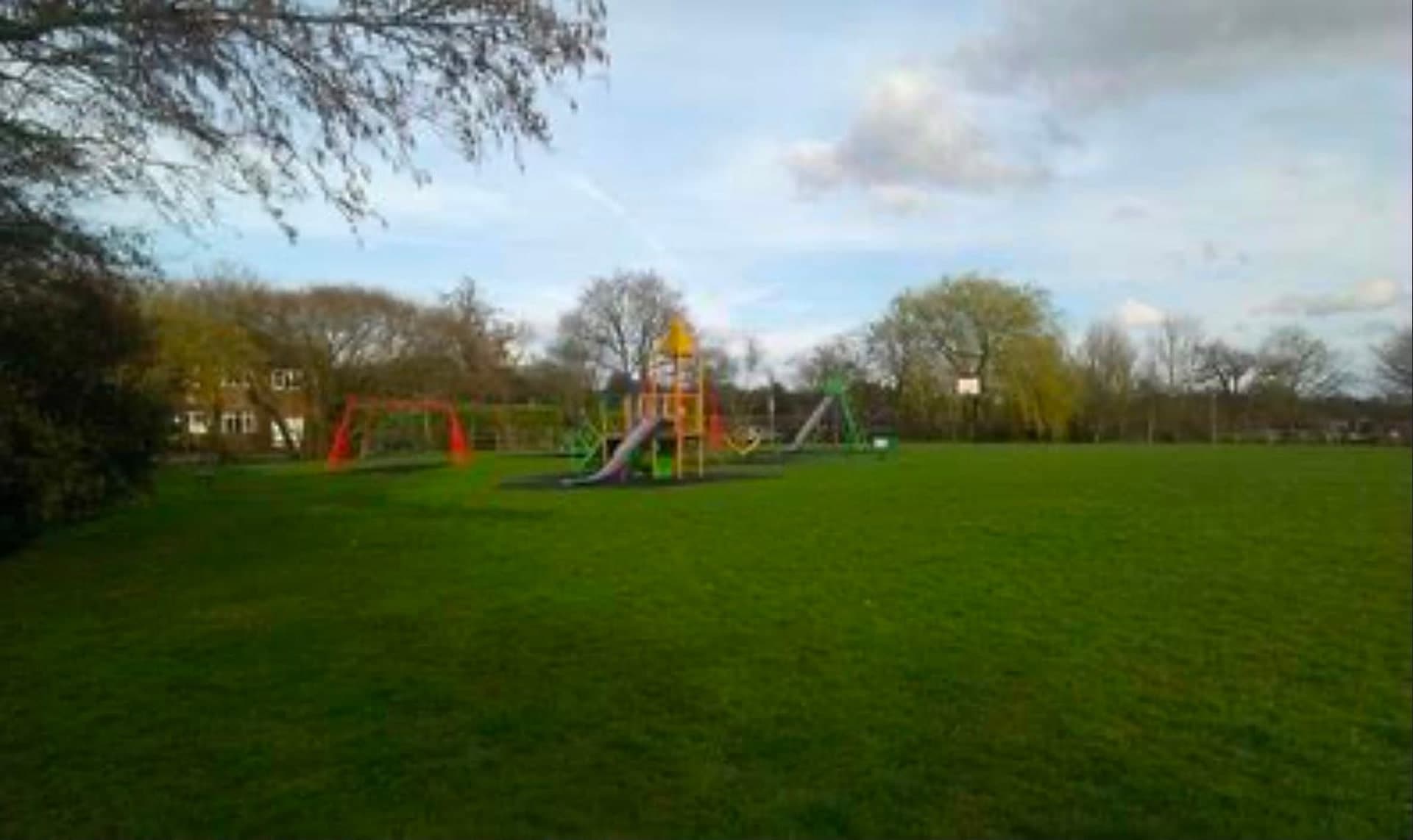 Swings and a climbing frame at the treeline, with open playing field stretching away